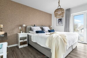 A bedroom with a large bed, bedside tables, a hanging light fixture, and a view through a glass door. - Holiday apartment at the marina (Damp)