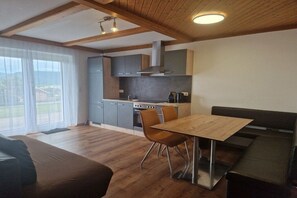 A modern kitchen with wooden beams, grey cabinets, and a dining area with a table and chairs. - Holiday apartment with 1 bedroom (Strasswalchen)