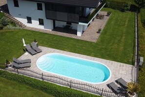 A modern house with a swimming pool, a patio with lounge chairs, and a well-maintained lawn. - Holiday apartment with 1 bedroom (Strasswalchen)