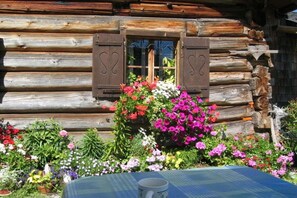 A log cabin with a window and shutters, surrounded by a variety of potted plants and flowers. - Holiday apartment with 1 bedroom (Strasswalchen)