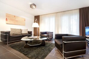 Ein modernes Wohnzimmer mit einer Couch, Sesseln, einem Couchtisch und einem Fernseher.
