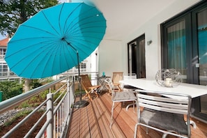 Ein Balkon mit Tisch und Stühlen, einem blauen Sonnenschirm und Blick auf Gebäude.