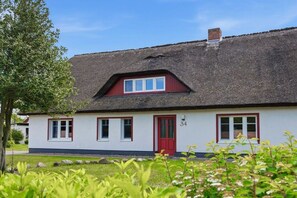 A traditional thatched-roof house with a red door and white walls, number 34, surrounded by greenery. - Holiday home in Wieck/Darß with sauna (Wieck\/Darß)
