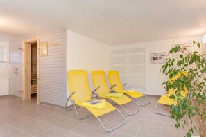 A waiting area with three yellow chairs, a wooden door, and a potted plant. - Holiday home in Wieck/Darß with sauna (Wieck\/Darß)