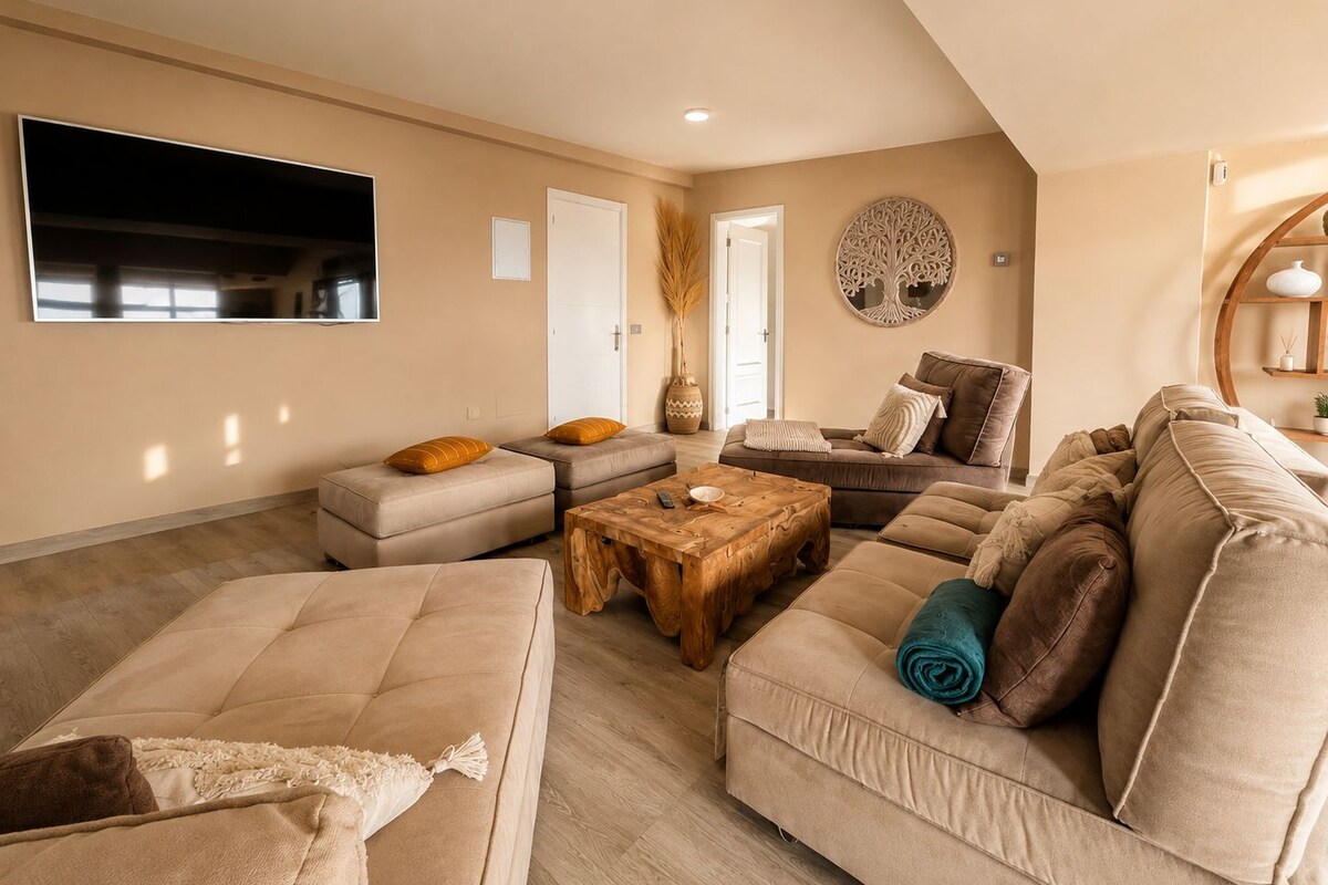 A spacious living room with a large flat-screen TV, a wooden coffee table, and multiple sofas.