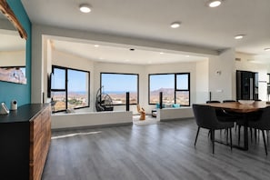 A modern interior with a dining area, large windows, and a view of the landscape.