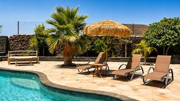 A poolside area with lounge chairs, a palm tree, and a thatched umbrella.