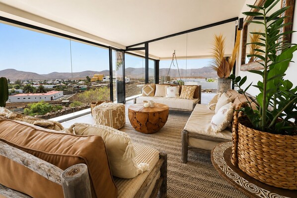 A spacious living area with a large window, a sofa set, a coffee table, and a potted plant.