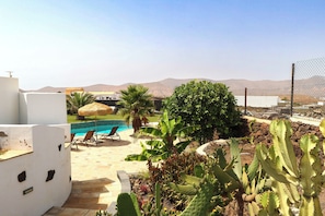 A pool area with a view of mountains, surrounded by cacti and palm trees.