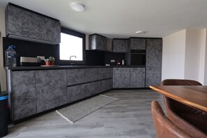 A modern kitchen with grey cabinetry, a built-in oven, and a dining area with a wooden table and chairs.