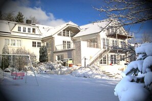 A snow-covered residential property with a staircase leading to a second floor, a swing set, and a clear sky. - Guesthouse "Vogelsang", Studio 2 (Sierksdorf)