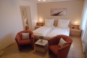 Ein Hotelzimmer mit zwei Betten, einem kleinen Tisch mit einer Vase, zwei Sesseln und einem Bild an der Wand.