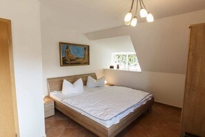 A bedroom with a wooden bed, a nightstand, a painting on the wall, and a window with a view. - Holiday home with 3 bedrooms (Born a. Darß)