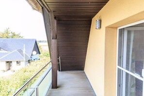A balcony with a wooden floor, a metal railing, and a view of a house with a sloped roof. - Holiday home with 3 bedrooms (Born a. Darß)