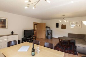 En stue med sofa, fjernsyn, pejs og spiseplads med bord og stole.
