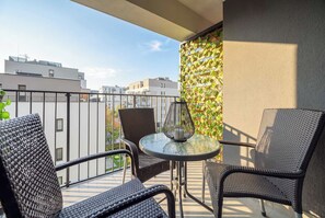 Een balkon met rieten stoelen en een glazen tafel, met uitzicht op een stadsbeeld.