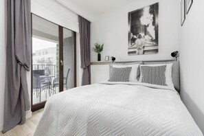 A modern bedroom with a large bed, grey curtains, a view of the balcony, and a black and white photograph on the wall. - Warsaw | Tolkiena 3 | Bright Studio | Balcony | Parking (Warszawa)