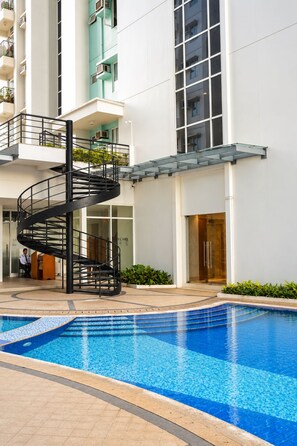 A modern building with a spiral staircase, a swimming pool, and a car dealership sign. - Deluxe Modern 3Bedroom Suite in Ermita Manila PH (Manila)