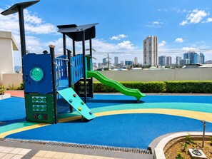 A playground with a slide and climbing area, surrounded by a blue play surface and a city skyline in the background. - Deluxe Modern 3Bedroom Suite in Ermita Manila PH (Manila)