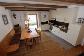 Un comedor acogedor con una mesa de madera y bancos, junto a una cocina con armarios blancos y un horno empotrado.
