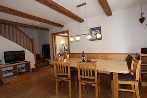A dining area with a wooden table and chairs, a television on a stand, and a staircase leading to another room.