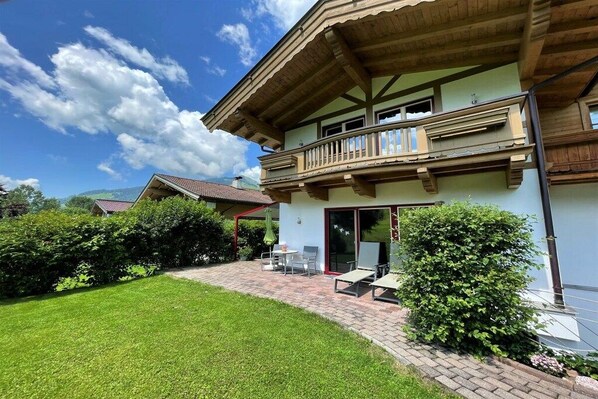 A two-story building with a balcony, a paved patio, and a well-maintained lawn.