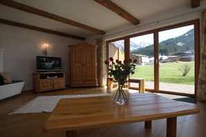 Una habitación con una mesa de madera, televisor, armario y ventana con vistas a montañas.