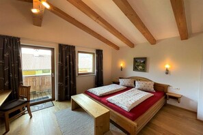A bedroom with a wooden bed, a bench, a chair, a bedside table, and a window with curtains.