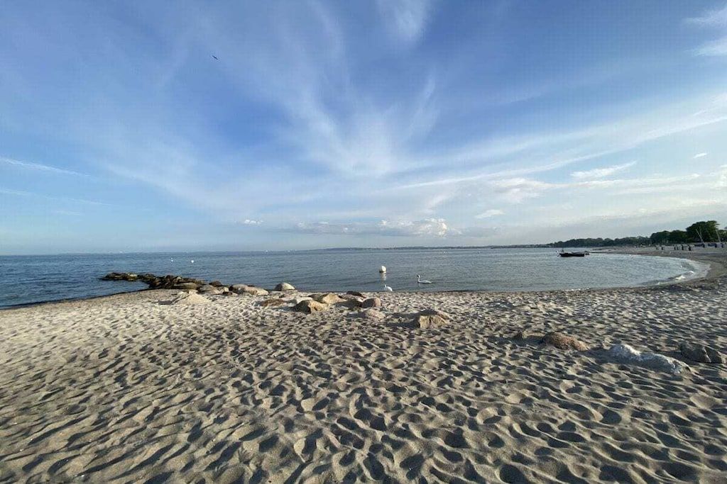 A beach with a clear sky, calm sea, and a rocky shoreline.