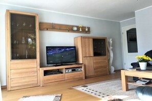 Un salon comprenant un téléviseur, des meubles en bois, une étagère décorative et une statue.