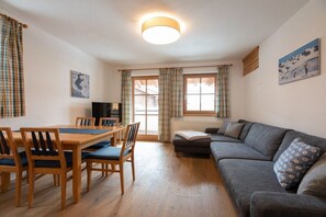 A cozy living room with a wooden dining table, chairs, a grey sofa, and a television. - Holiday apartment with 1 bedroom (Maria Alm)