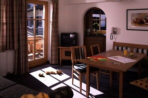 A room with a dining table, chairs, a television, and a window with curtains. - Holiday apartment with 1 bedroom (Maria Alm)
