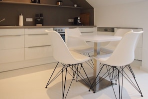 A modern kitchen with white cabinetry, a central island, and a dining area with white chairs and a table. - Holiday apartment with 1 bedroom (Timmendorfer Strand)