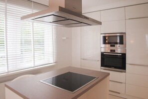 Een moderne keuken met een ingebouwde oven, een fornuis en een raam met zonwering.