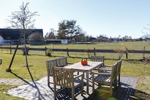 An outdoor patio with a table and chairs, a wooden fence, and a grassy field in the background. - Holiday apartment with 2 bedrooms (Wieck a. Darß)