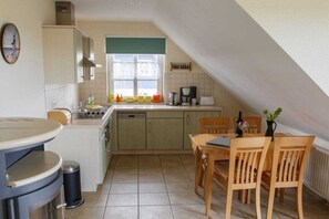 A compact kitchen with a dining area, featuring a window, a sink, and a stove. - Holiday apartment with 2 bedrooms (Wieck a. Darß)
