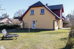 A two-story house with a red roof and yellow walls, a front door, and a small front yard with a lawn and a bench. - Holiday apartment with 2 bedrooms (Wieck a. Darß)