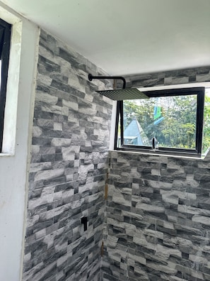 A bathroom with a stone-patterned wall, a window, and a shower head. - Pachamama Pyramid 5 (La cruz)