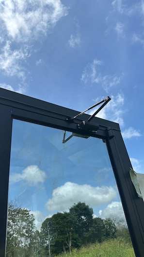 A window with a wiper mechanism, clear sky, and reflections of trees and clouds. - Pachamama Pyramid 5 (La cruz)