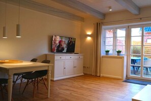 Ein Essbereich mit Tisch und Stühlen, einem weißen Schrank, einem an der Wand befestigten Fernseher und einem Fenster mit Vorhängen.