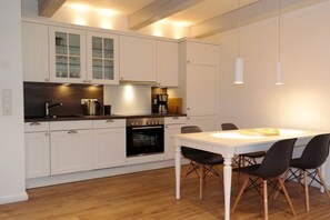 A modern kitchen with white cabinetry, a built-in oven, and a dining area with a white table and black chairs. - 3 Barbados in the Boldix House (Wyk-Boldixum)