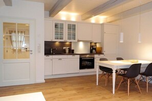 Eine moderne Küche mit weißen Schränken, einem Esstisch mit Stühlen und einem sichtbaren Backofen.