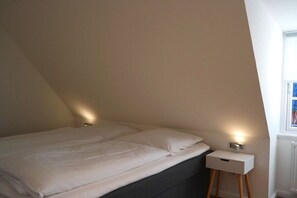 Een slaapkamer met een bed, nachtkastje en een raam.