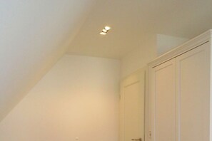 Ein Zimmer mit schrägem Dach, einer weißen Tür und einer eingelassenen Deckenleuchte.