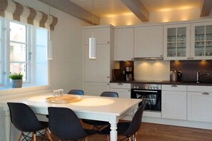 Une cuisine moderne avec des meubles blancs, une table à manger avec des chaises et une fenêtre avec des stores.