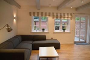 Un salon moderne avec un canapé d’angle, une table basse et une grande fenêtre agrémentée de rideaux.