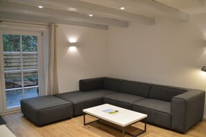 Una sala moderna con un sofá seccional gris, una mesa de centro blanca y un ventanal corredizo que da a un espacio al aire libre.