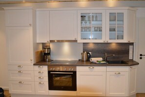 Una cocina con armarios blancos, una estufa de acero inoxidable, horno empotrado, cafetera y un lavamanos.