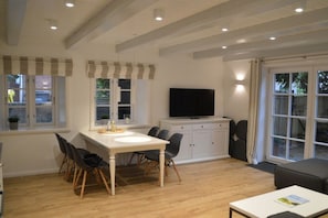 A modern kitchen with a dining table, chairs, a television, and cabinets. - 1 Aruba at Haus Boldix (Wyk-Boldixum)