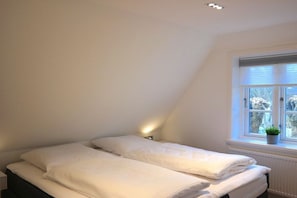 Un dormitorio con cama, mesita de noche, ventana con persianas y planta en maceta.